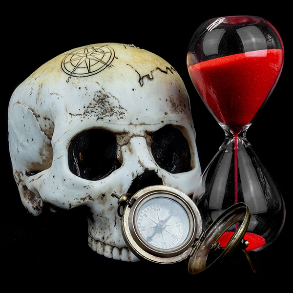 Ein Kompass und eine Sanduhr mit rotem Sand neben einem Schädel aus Kunstharz