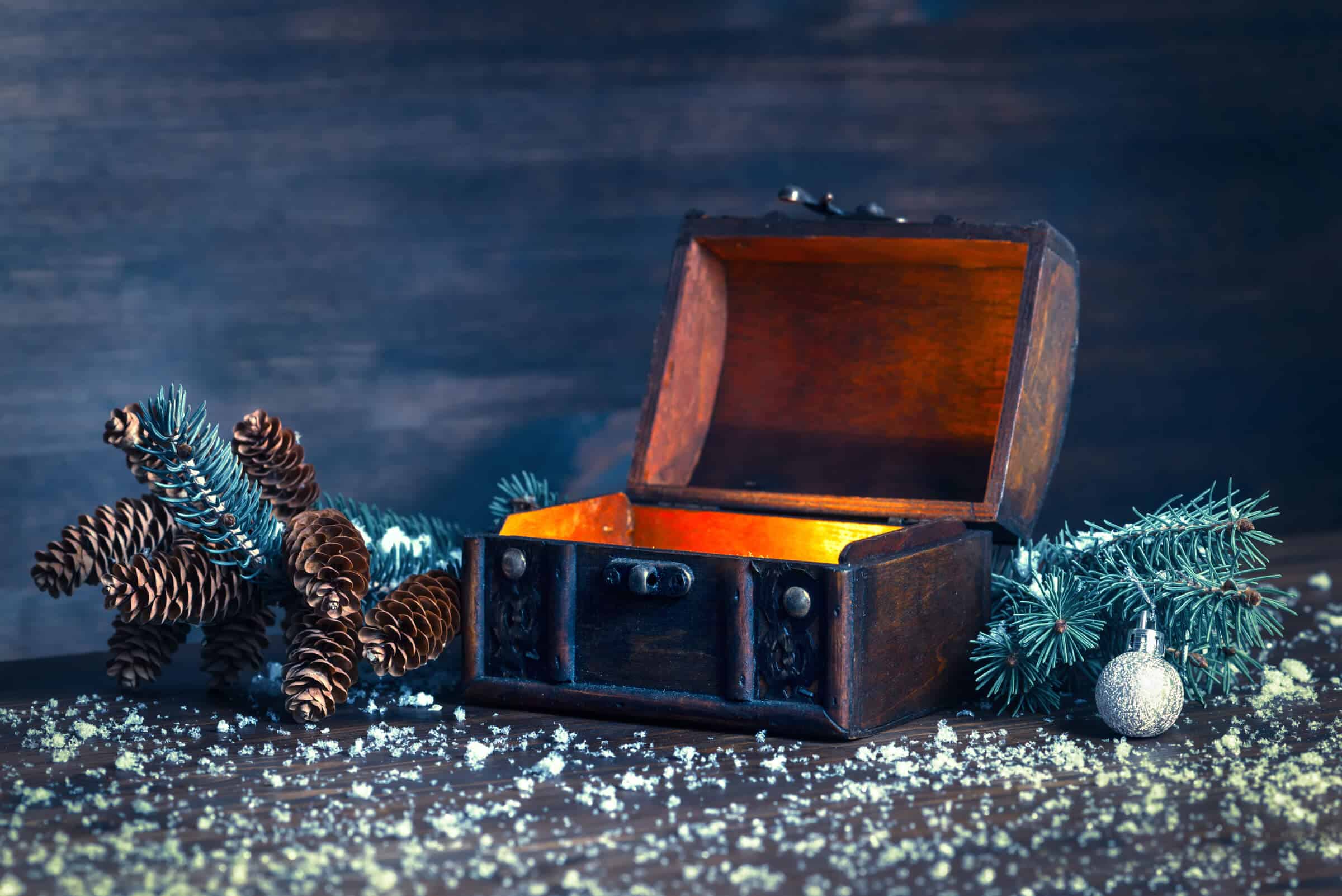 christmas-escape-academy-background Eine kleine Schatztruhe zwischen Tannenzweigen, die aus dem Inneren heraus zu glühen scheint.